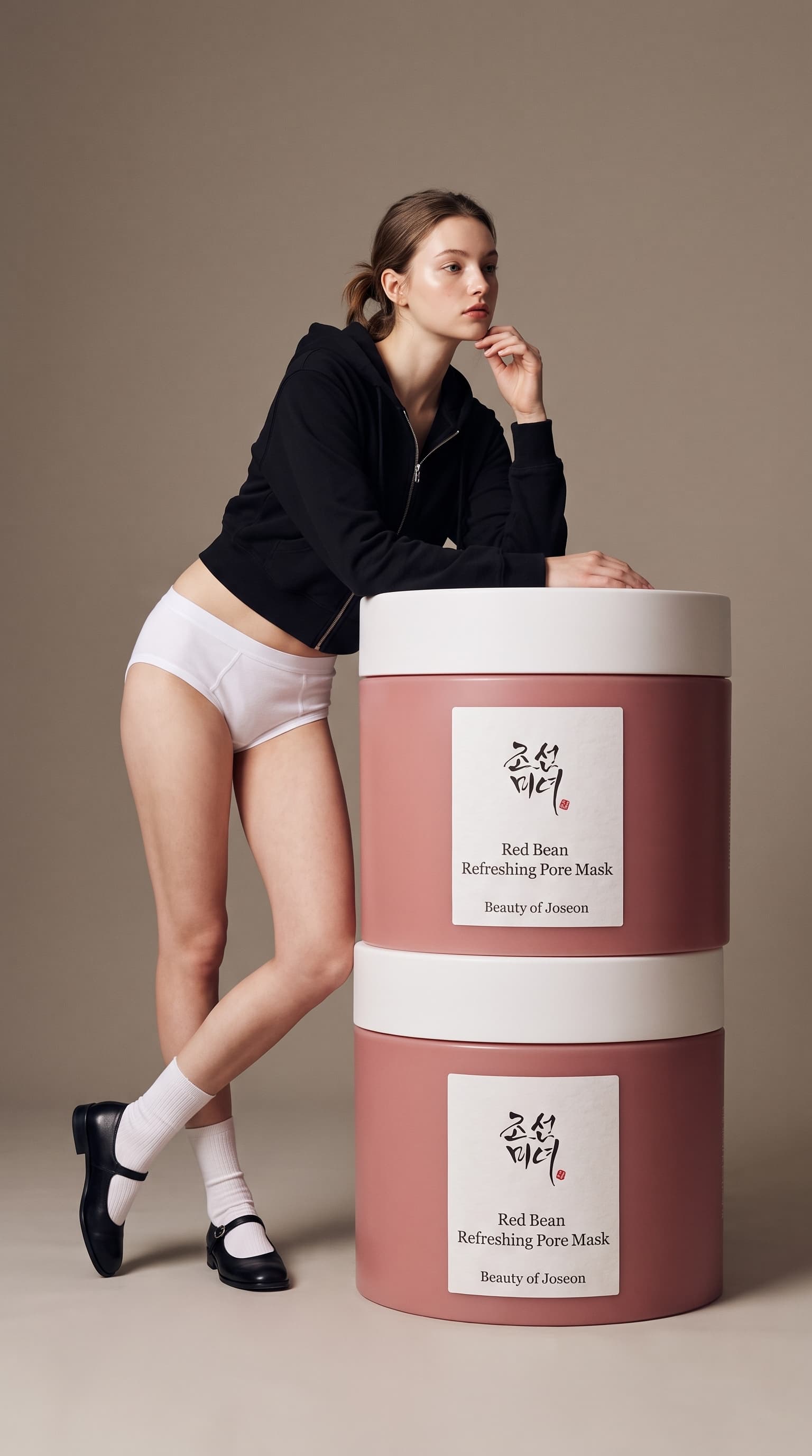 Woman in a black cropped hoodie leaning on two giant stacked pink skincare jars, made with Nano Banana Pro