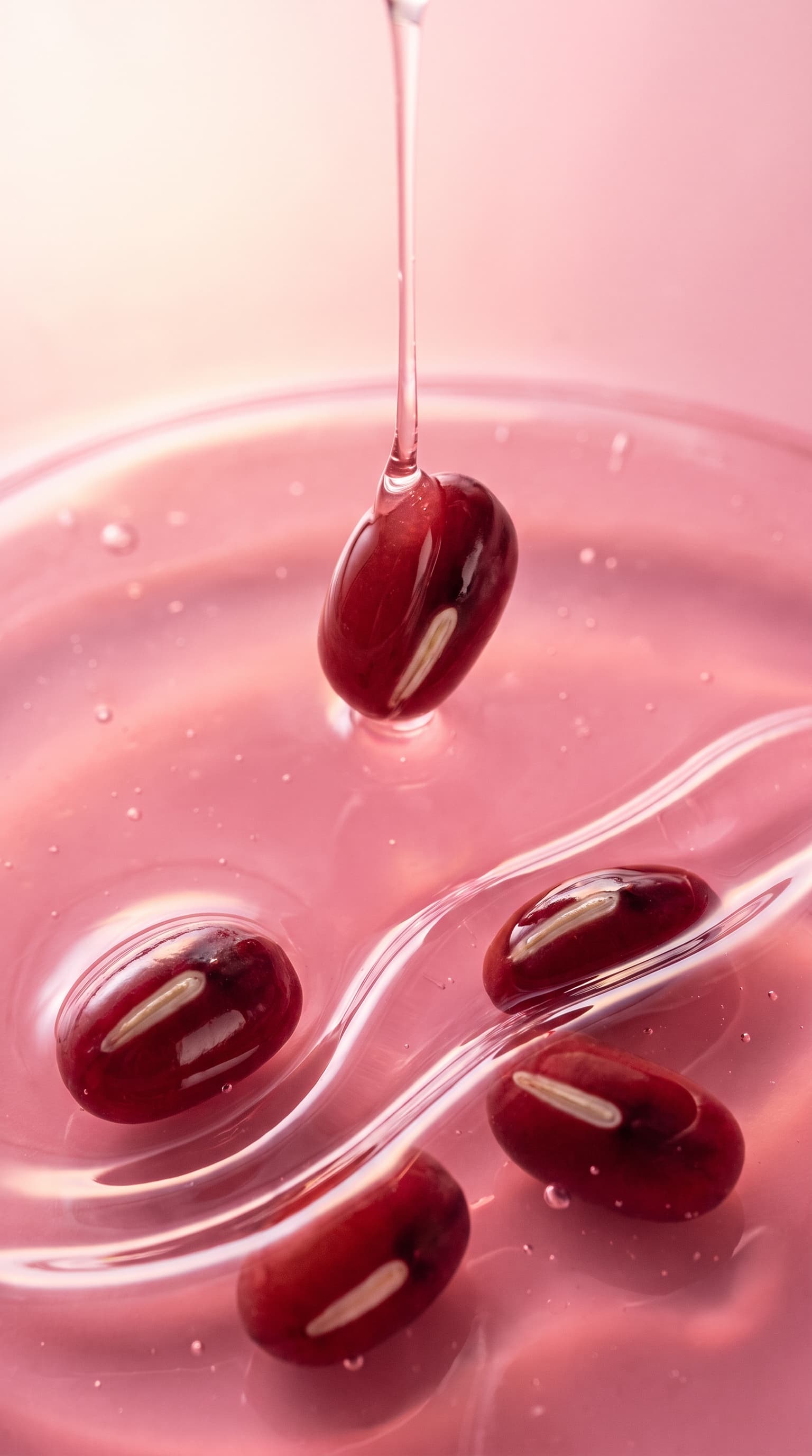 Red beans sinking into glossy pink gel with a strand of gel dripping onto one, made with Nano Banana Pro