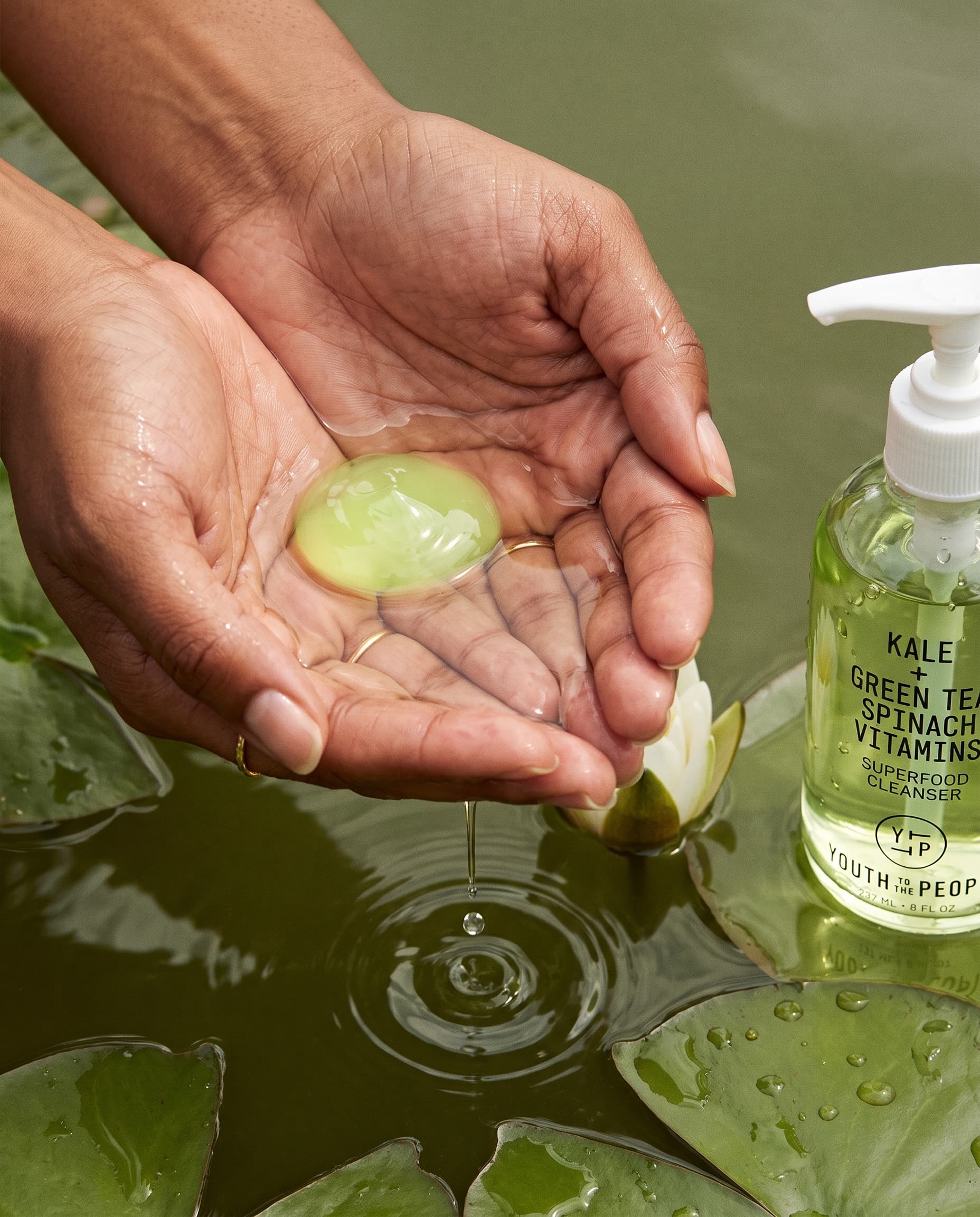 Wet cupped hands holding a disc of green gel over pond water, a cleanser bottle on a lily pad beside them, made with Nano Banana Pro