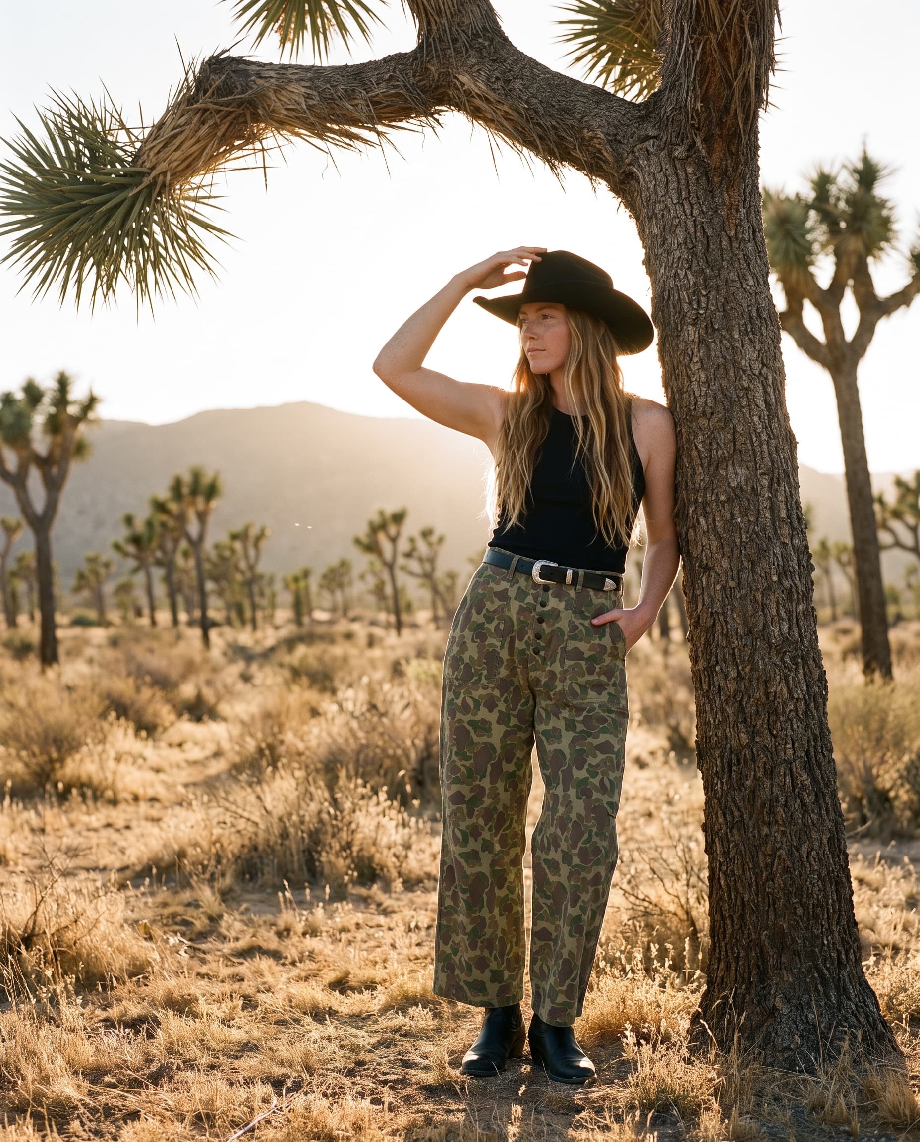 Woman in camo pants, black tank and black western hat leaning on a Joshua tree at golden hour, made with Nano Banana Pro