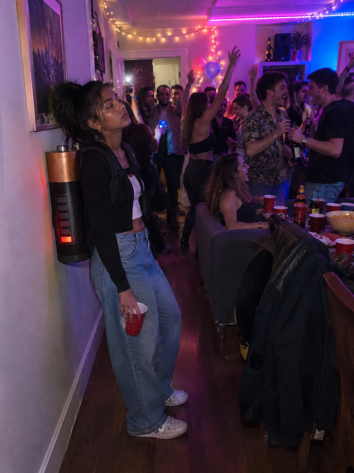 Woman at a house party with an empty battery strapped to her back, leaning on a wall, made with GPT Image 2.5 Flare