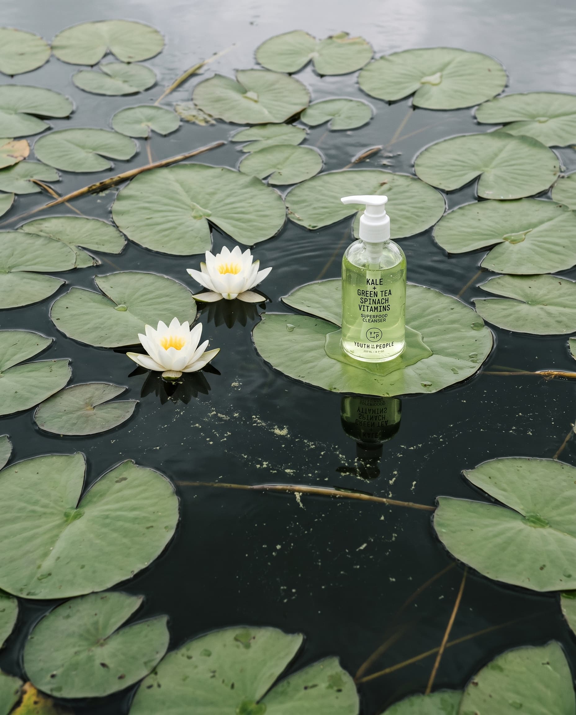 Overhead view of a dark pond with lily pads, two white water lilies and a small green cleanser bottle on one pad, made with Nano Banana Pro