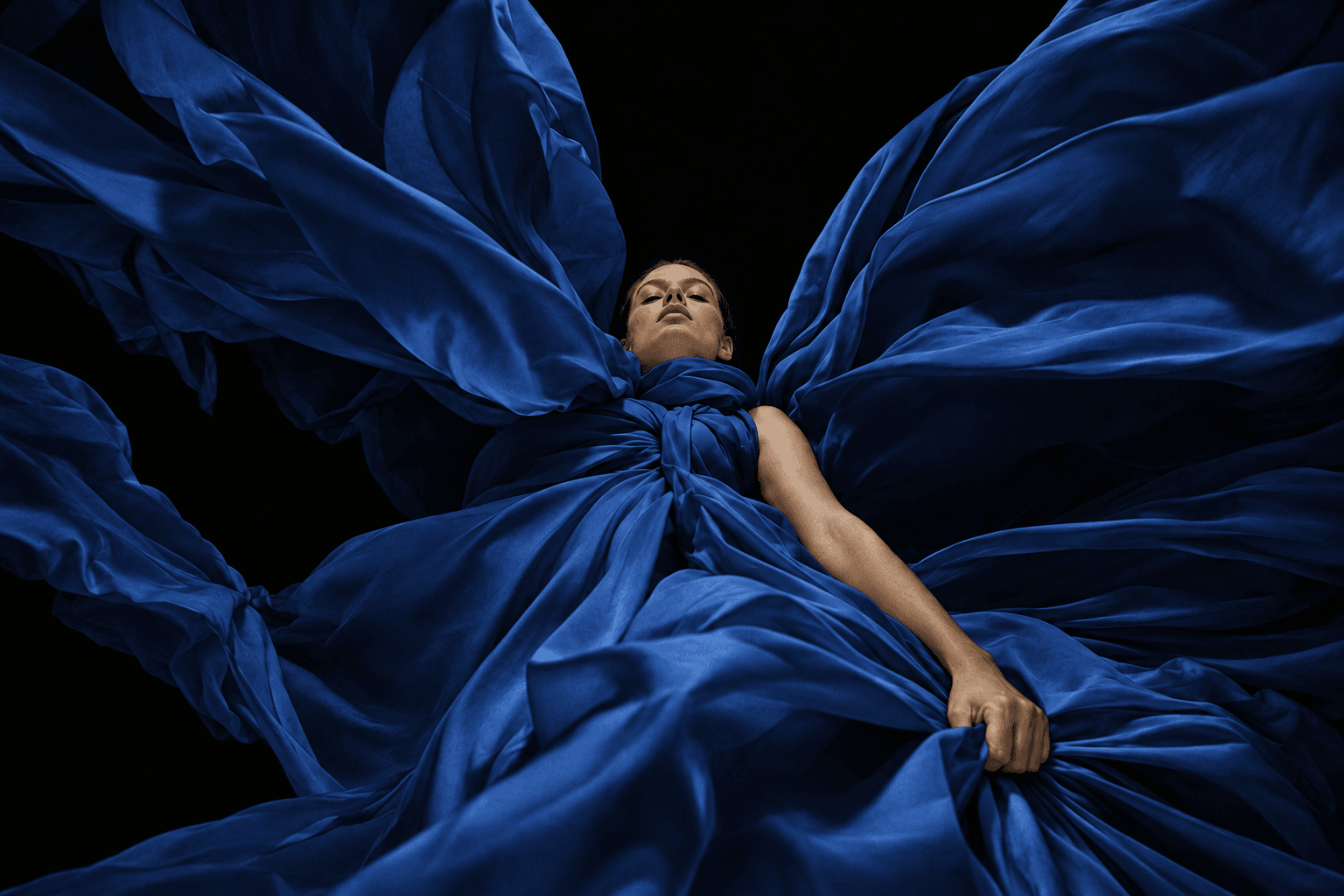 Woman wrapped in billowing deep blue silk seen from directly below against black, made with GPT Image 2.5 Sunburst