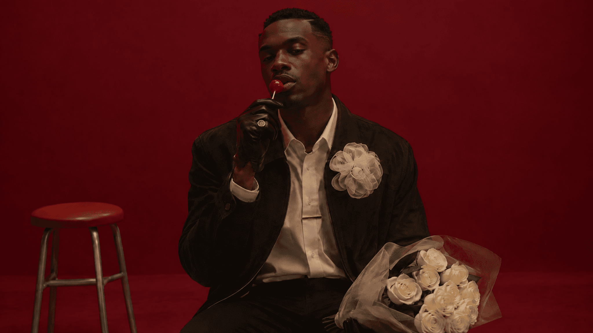 Man in a suede jacket with an organza flower against a burgundy wall, fully lit, made with GPT Image 2.5 Sunburst