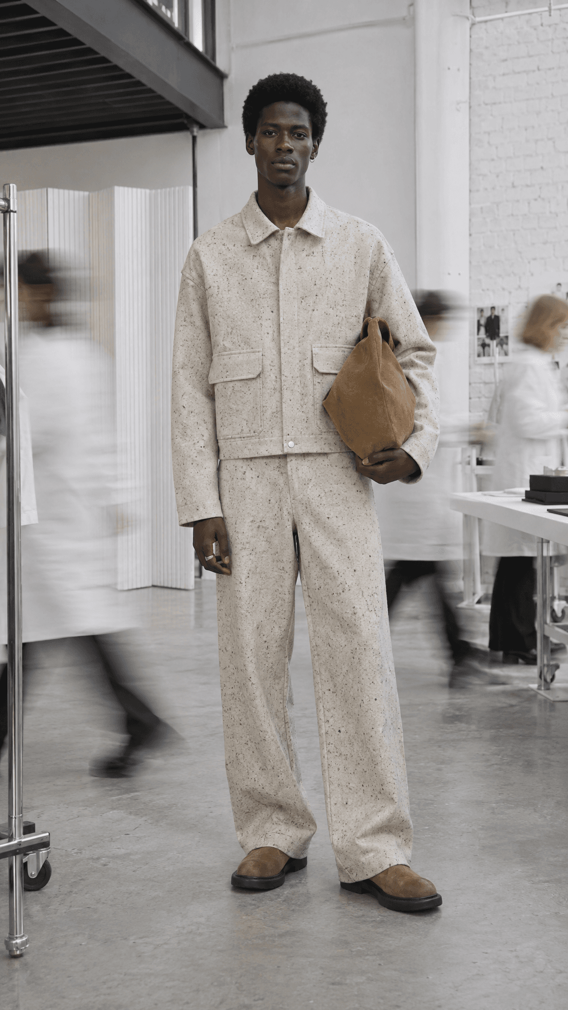 Model in a speckled oatmeal suit in a white loft, staff in white coats blurred around him, made with GPT Image 2.5 Sunburst
