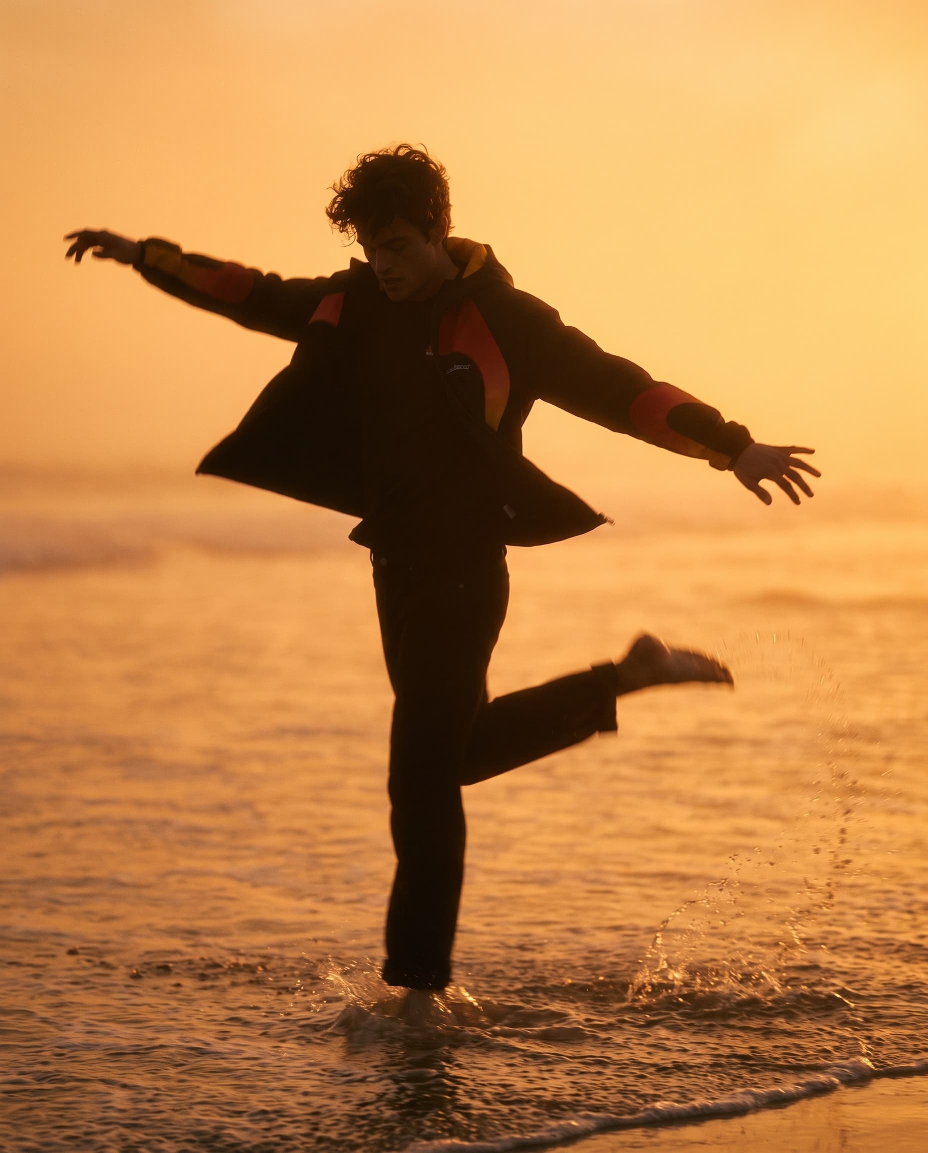 Silhouette of a young man kicking up water in the surf with his arms out, inside thick orange haze, made with Nano Banana Pro