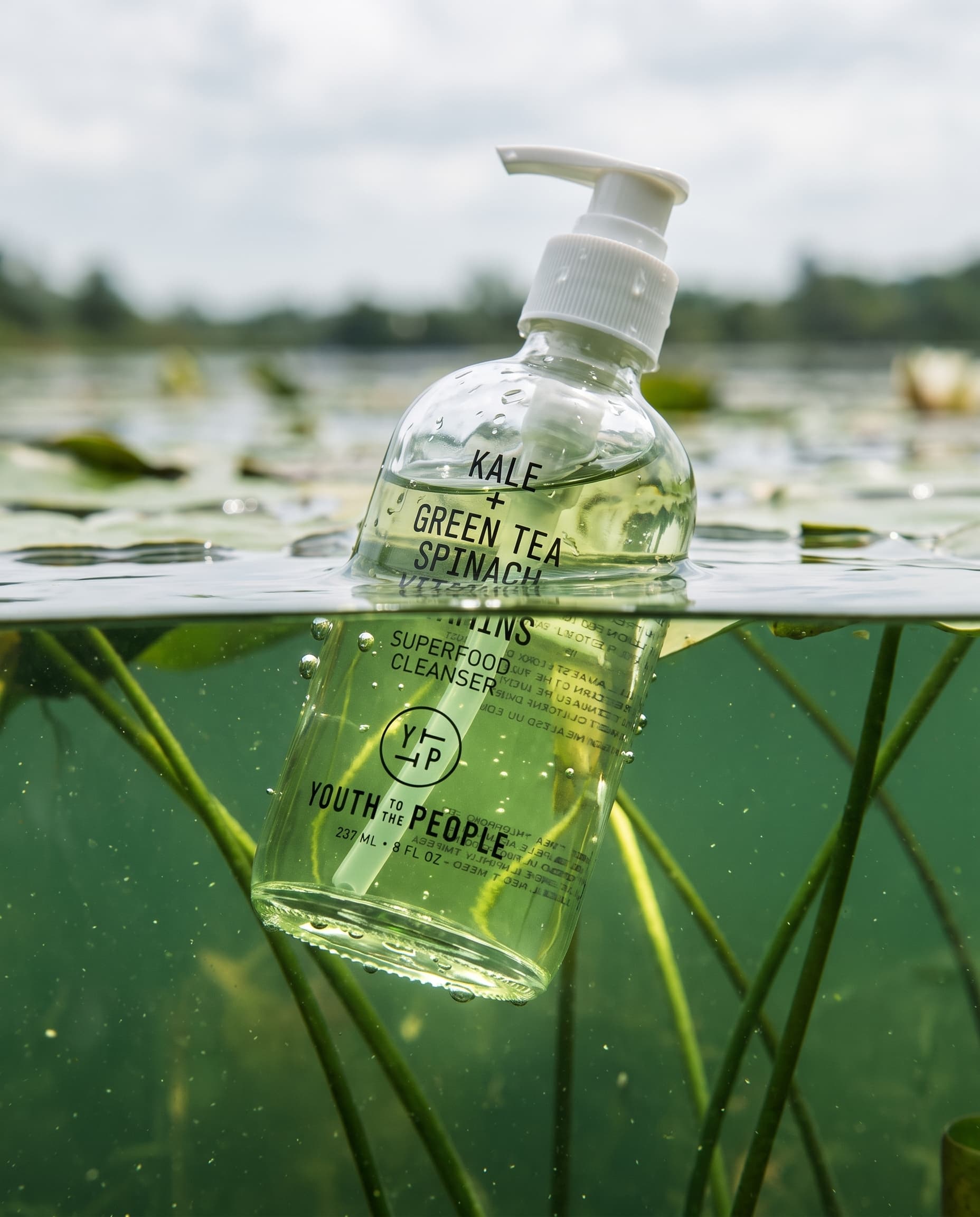 Split-level view of a clear cleanser bottle half underwater among lily stems, made with Nano Banana Pro